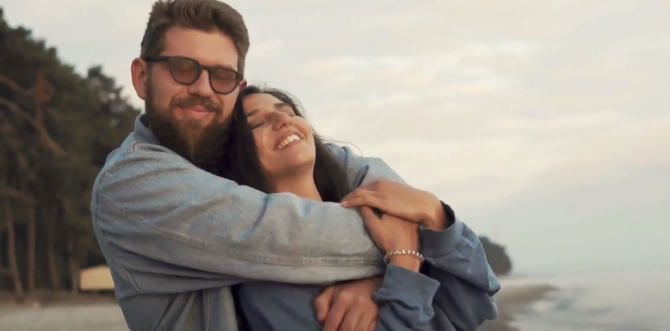 Photo of a guy and a girl outside, with the guy hugging the girl from behind