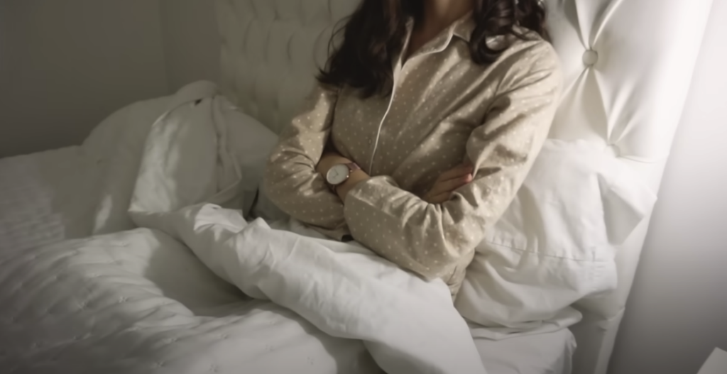 Photo of a girl sitting on a bed, leaning back against the headboard with her arms crossed